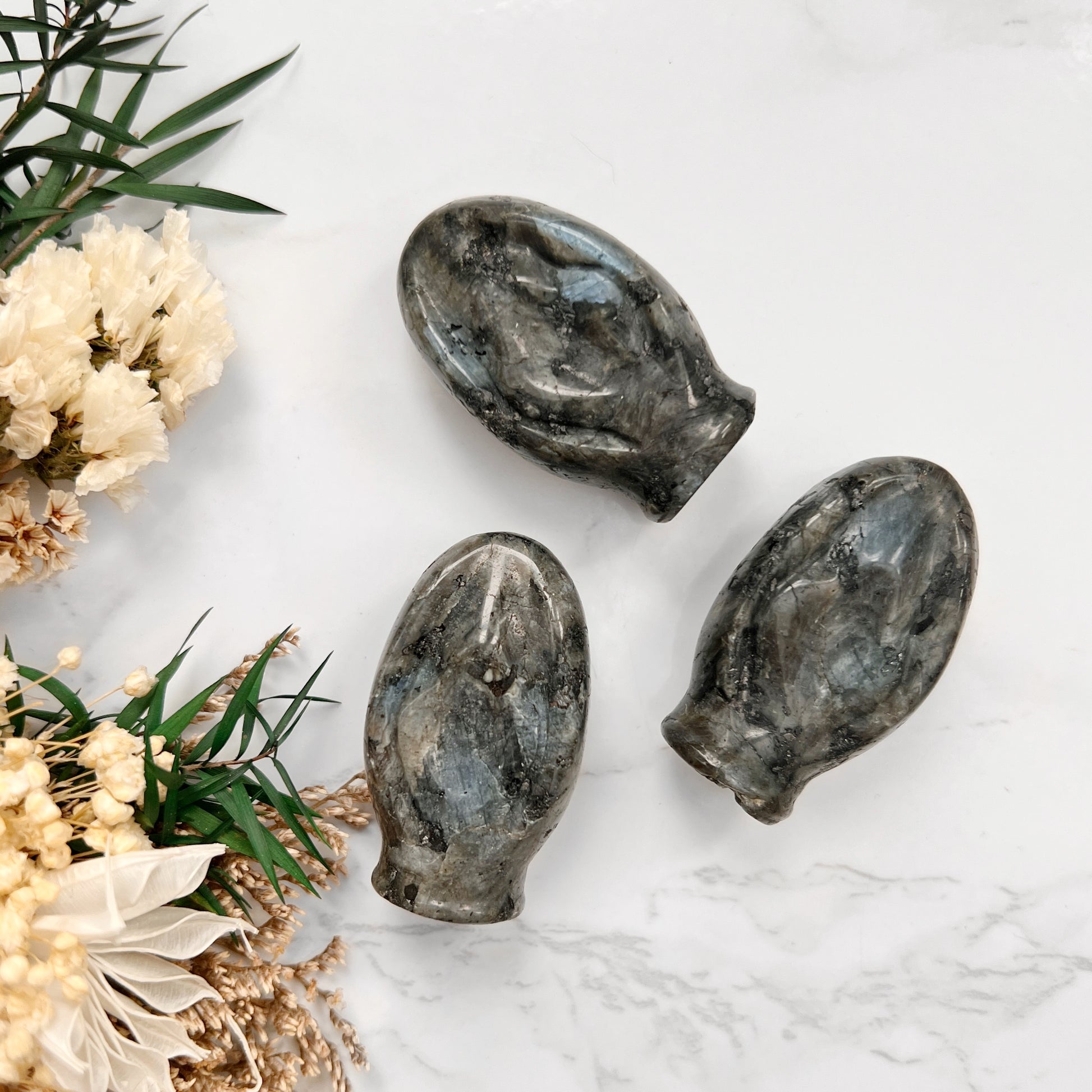Triple Grounding Force: A striking display of three Larvikite crystal vulva shapes, each embodying the protective and grounding energy of this gemstone. The deep, earthy hues of Larvikite symbolize its connection to the Earth's stabilizing and grounding properties.