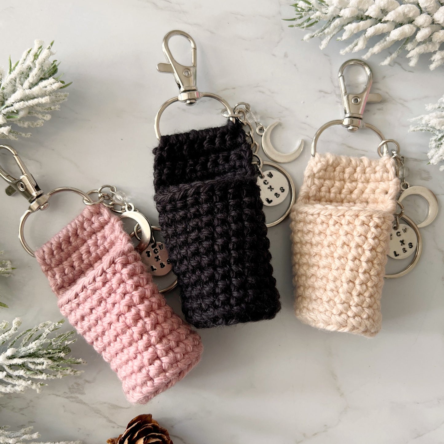 Three crochet lip balm holders and keychains in pink, black, and beige, from Lather and Soul