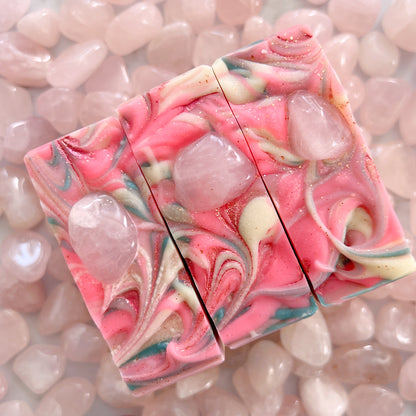Three crystal rose quartz soaps sit side by side in an array of rose quartz crystals.