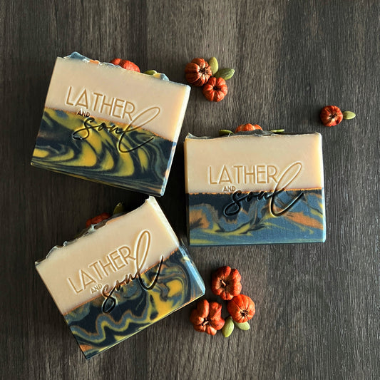Three bars of Lather and Soul soap on a dark wooden surface with decorative elements.