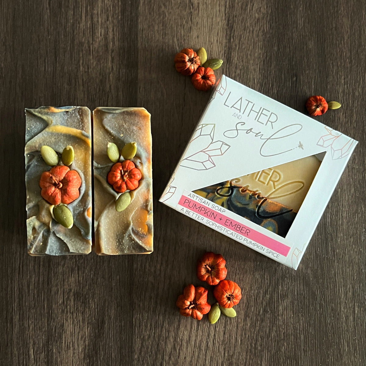 Two soap bars with decorative elements on a wooden surface, accompanied by a box labeled 'Lather & Soul'.