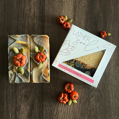 Two soap bars with decorative elements on a wooden surface, accompanied by a box labeled 'Lather & Soul'.