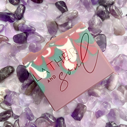 Artisan Crystal Bar Soap with Genuine Amethyst are swirled purples, pinks, whites, and greens and sits on amethyst