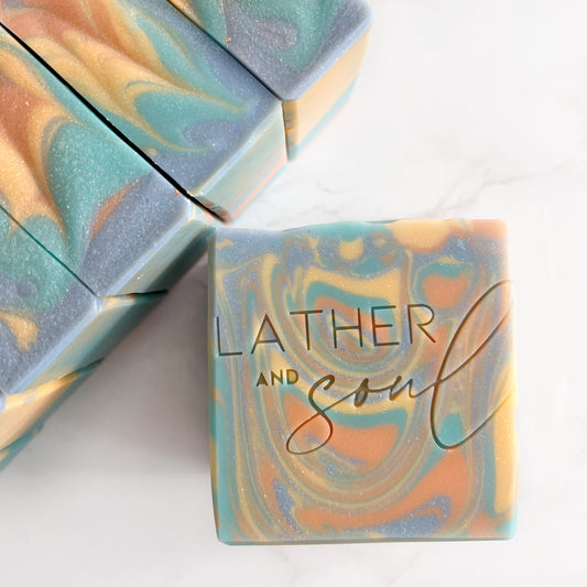 Handmade artisan soap with blue, green, orange, and gold swirls, "Earth Sun Fusion."