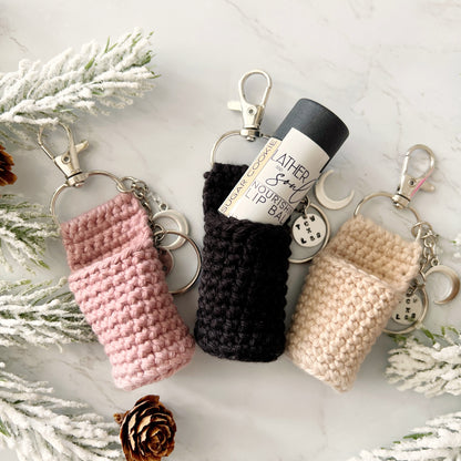 Three crocheted keychains in pink, black, and beige, custom fit for Lather + Soul lip balms
