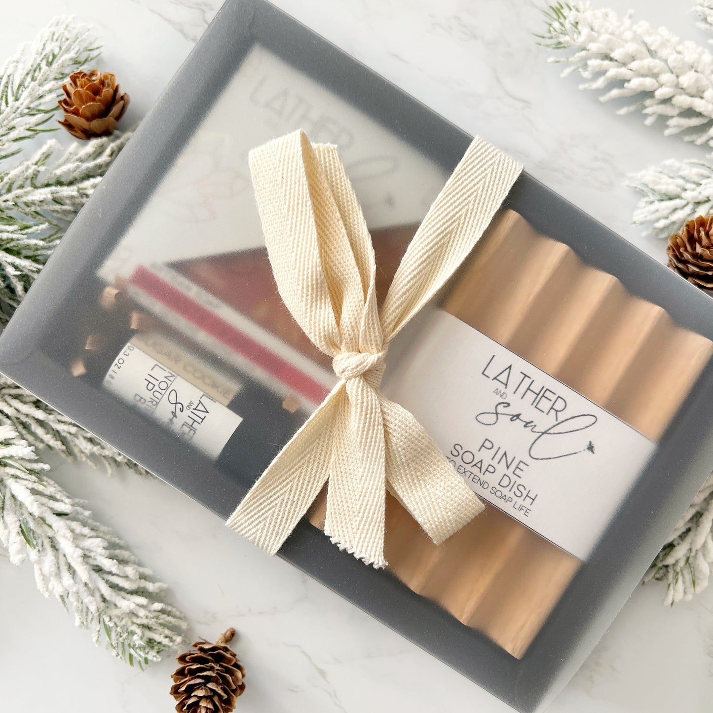 Gift set with soap, soap dish, and lip balm in a box with a bow, surrounded by decorative elements.