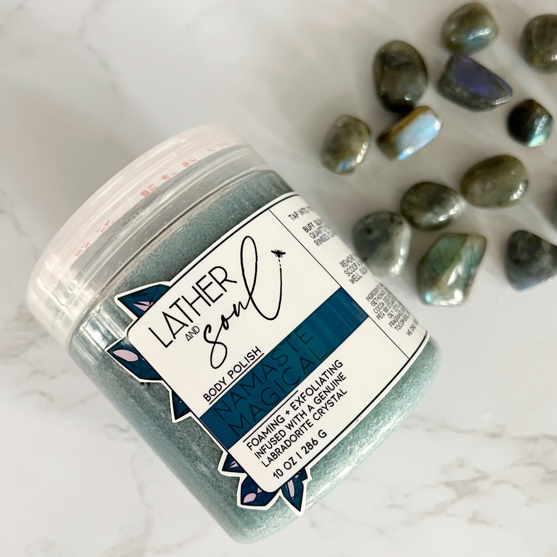 Jar of Lather & Soul body scrub with labradorite stones on a marble background