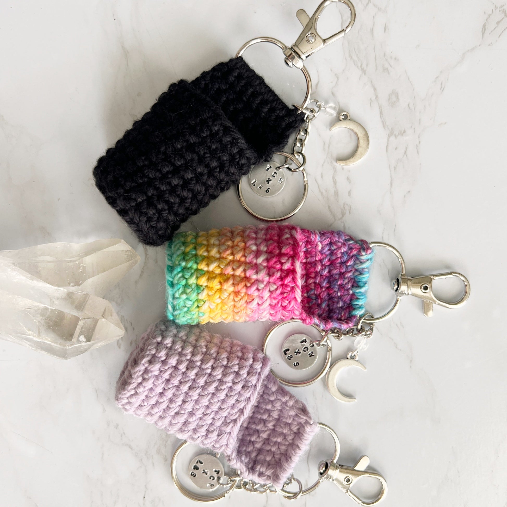 Three crocheted keychains in black, rainbow, and pink, custom for Lather and Soul lip balms