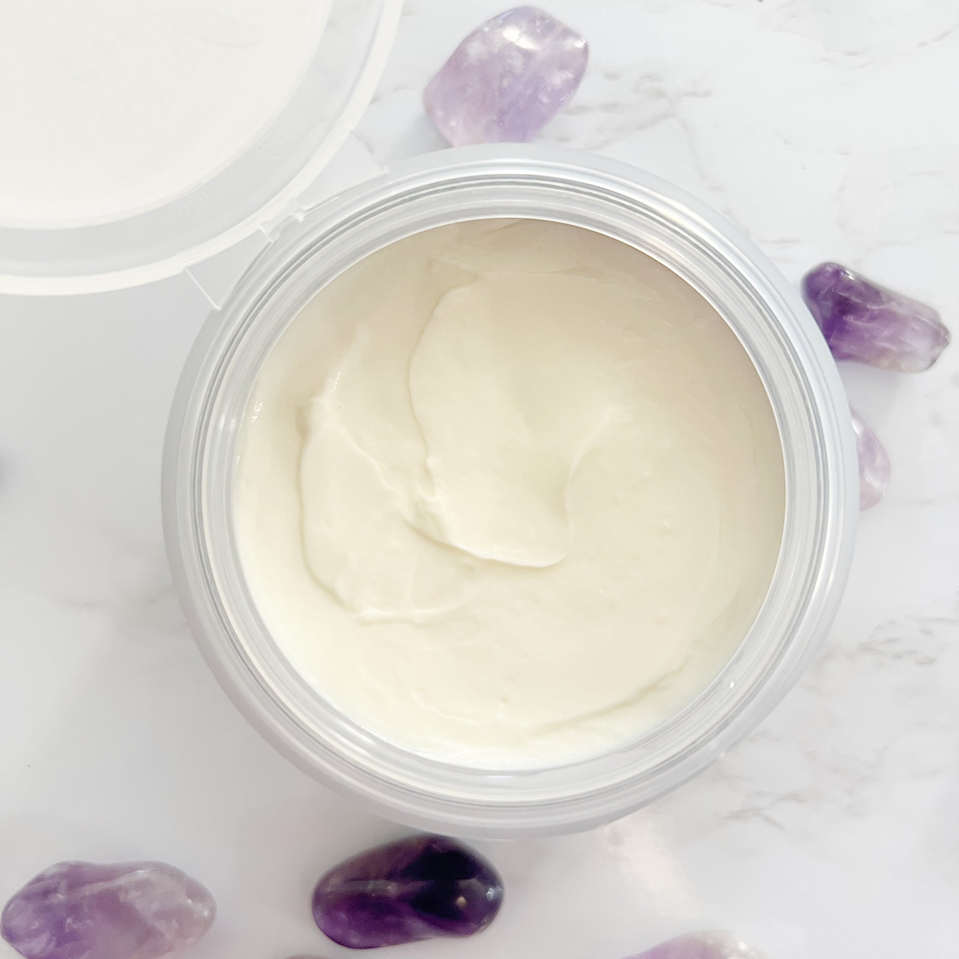 Body crème by Lather and Soul Skincare sits on white table with amethyst.