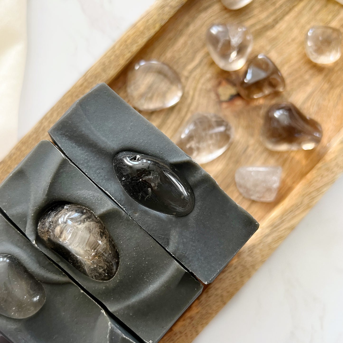 Namaste Protected Crystal Soap with Genuine Smoky Quartz are shown on a wood tray on a  white table.