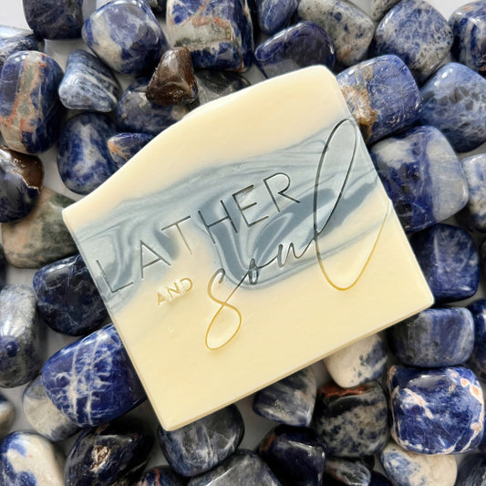 A marbled Namaste Intuitive Crystal Soaps with Genuine Sodalite sits on an array of sodalites