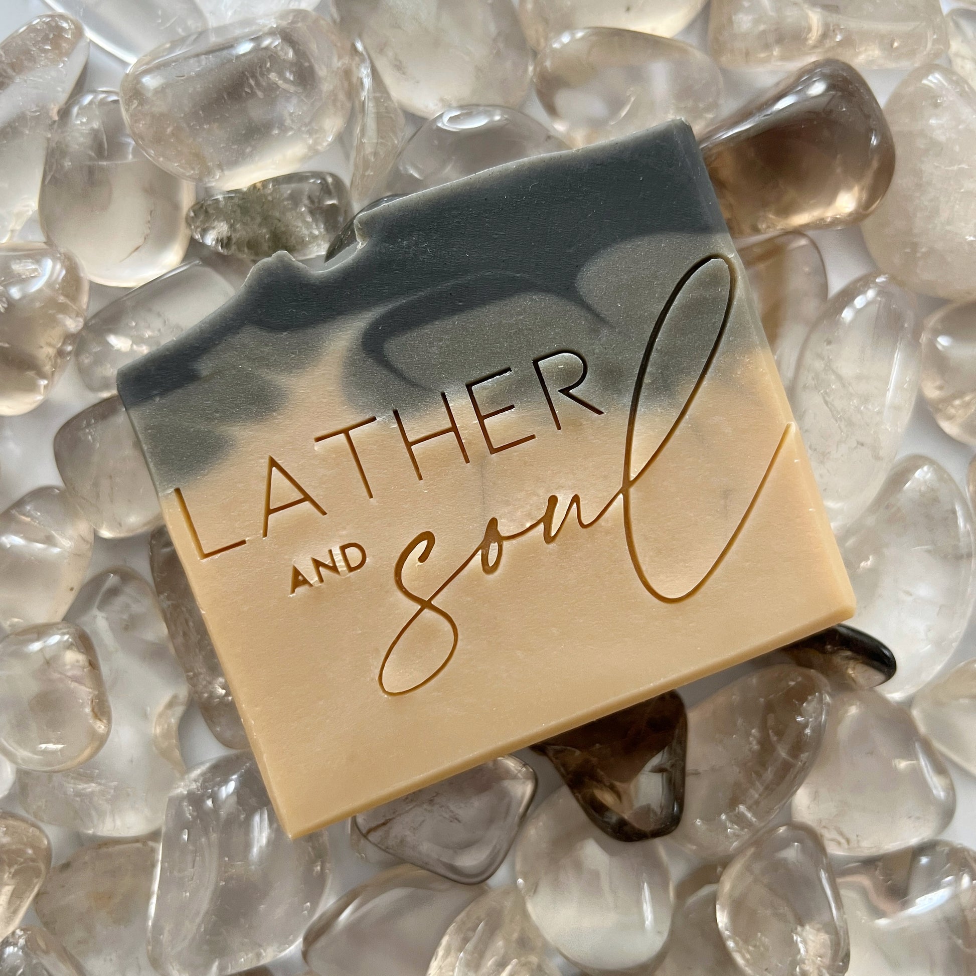 An artisan crystal soap by Lather and Soul Skincare is colored black and brown and sits on a pile of smoky quartz crystals.