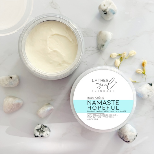 Luxurious body crème by Lather and Soul Skincare, surrounded by rainbow moonstones on white table, in Namaste Hopeful Scent